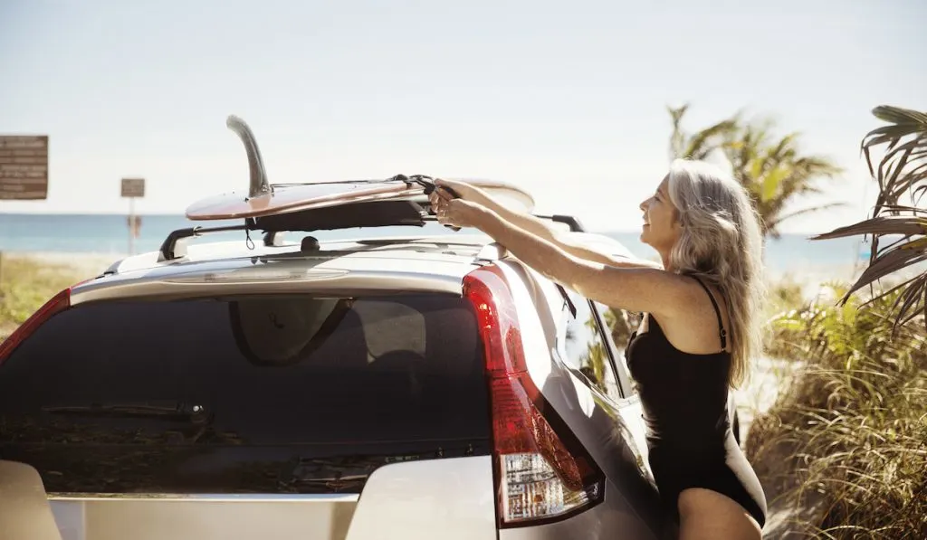 woman putting a surfboard on top of her car