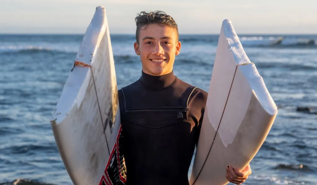 young lad holding a surfboard broken in half