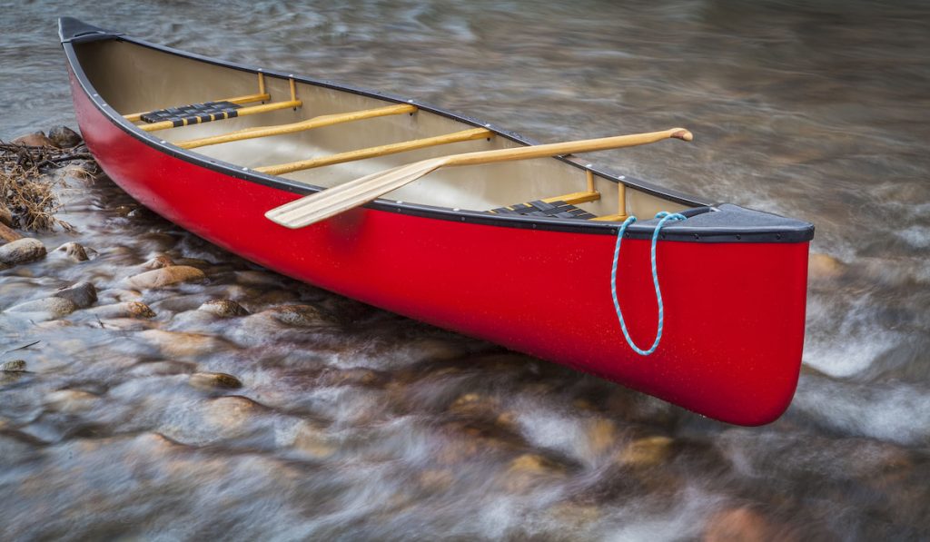 red tandem canoe with a paddle on a shallow rocky river
