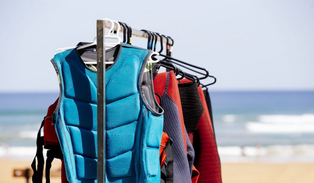 A row of wetsuits hanging on a rack at a beach
