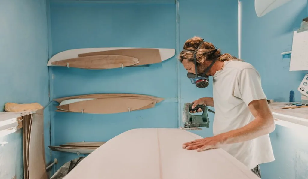 Man in respirator polishing surf board in workshop