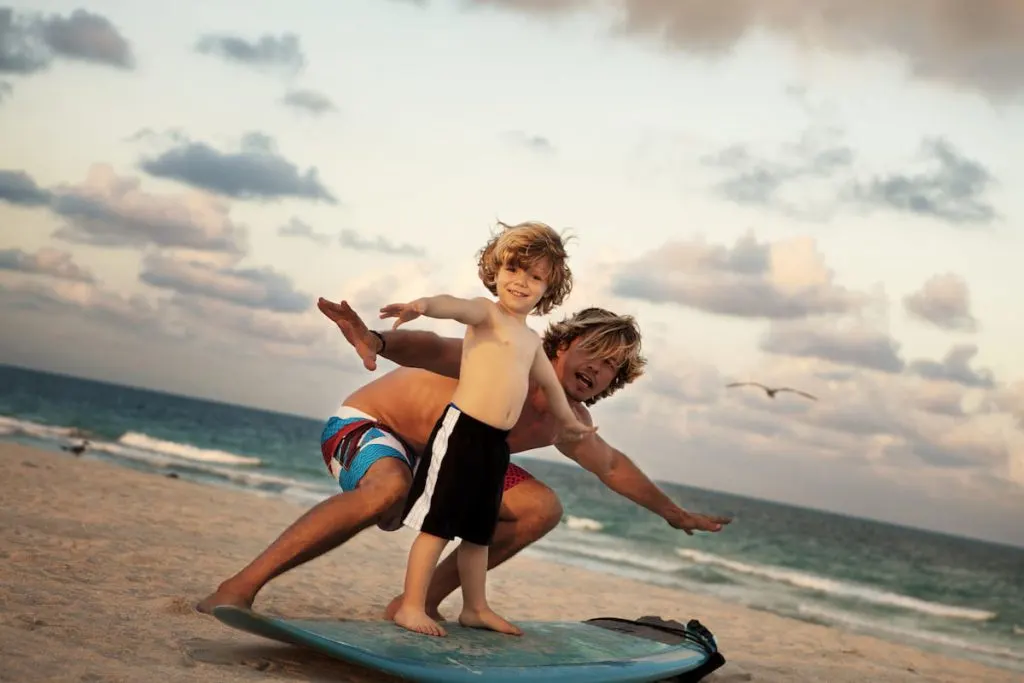 Portrait Of Father Teaching Son To Surf At Beach