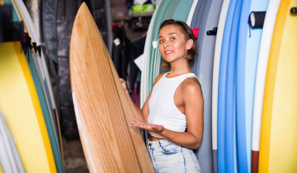 Portrait of cheerful positive smiling woman with board for surfing in the shop