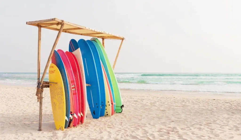 Set of different color surf boards in a stack by ocean