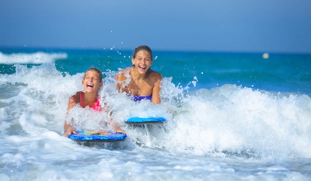 Two cute girls having fun with surfboard in the ocean