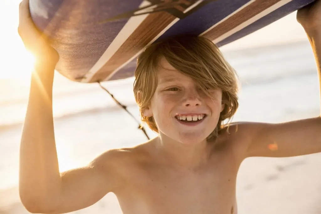 boy-carrying-surfboard-over-head-smiling