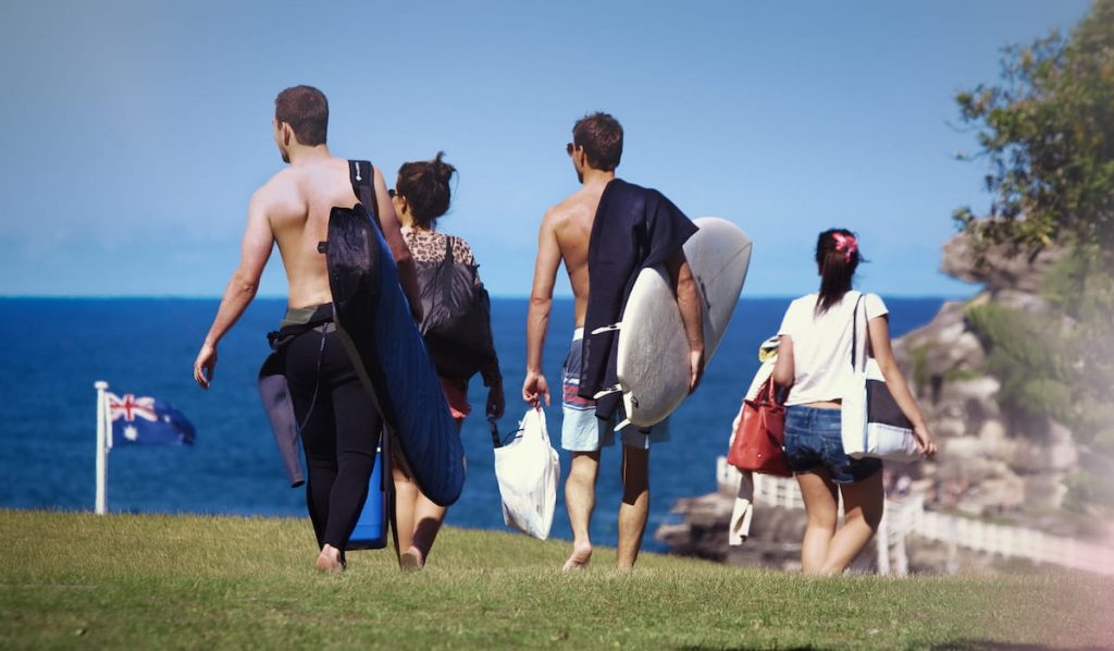 young surfers with surfboard bag walking towards the beach
