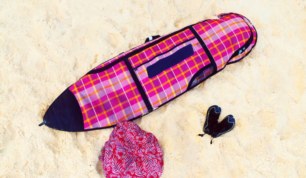 Surf bag with a board, reef boots on a white sand