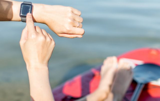 Woman using smart watch while paddleboarding on the lake - ee220813
