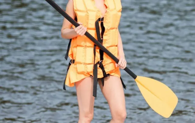 Young woman in life vest standing with oar and standup paddleboard on the beach - ee220813