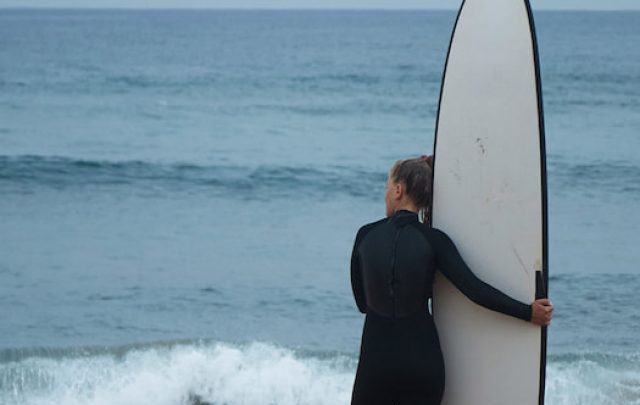 surf girl hugging her longboard on ocean shore and watching waves before surfing - ss220803