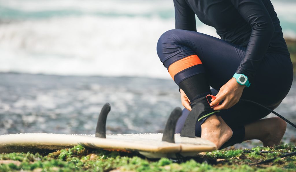 woman surfer trying leg leash with surfboard on seaside reef 