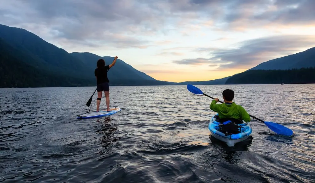 friends on lake kayaking and paddle boarding together 