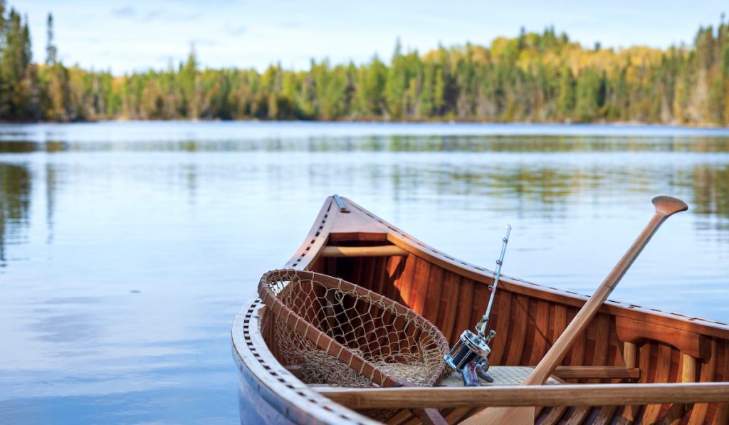 Closeup shot of wooden canoe with vintage fishing rod and net on the lake