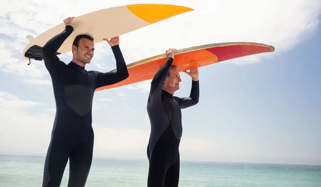 Happy father and son carrying surfboard over their head on the beach