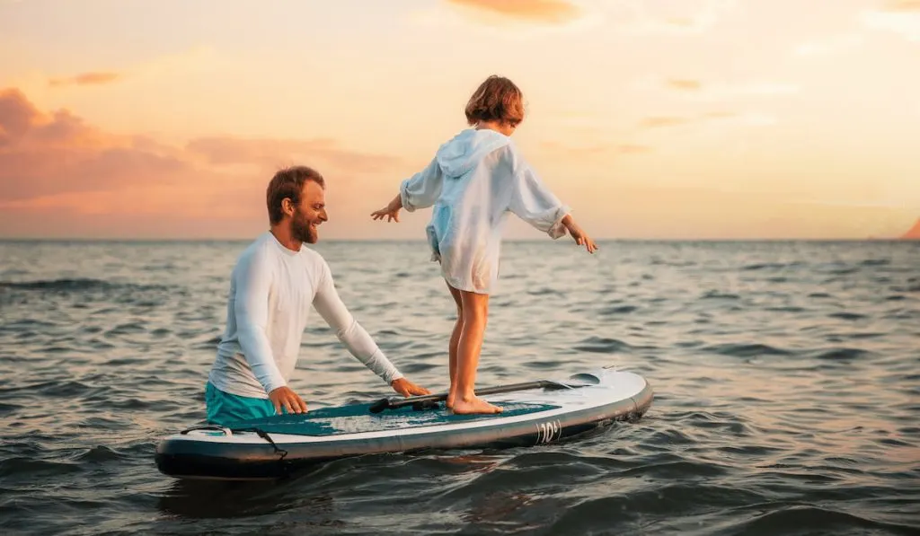 Instructor teaches the pre school girl to swim with a sup board