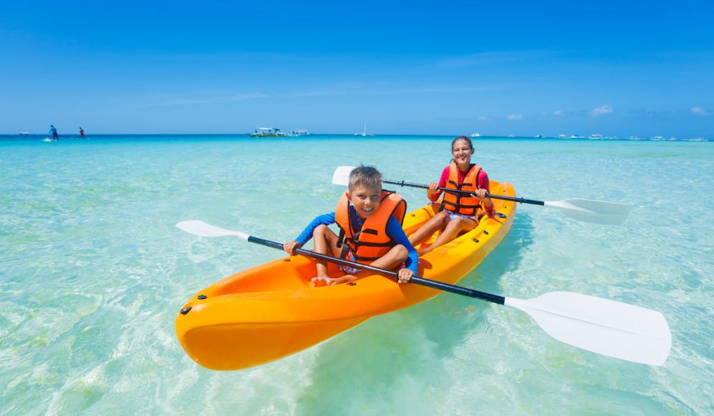 Kids enjoying paddling in orange kayak at tropical ocean water during summer vacation
