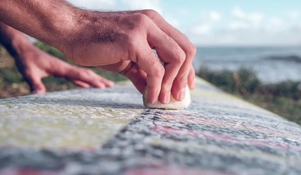 Side view crop hands of man spreading wax on surfboard