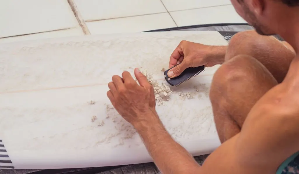 Surfer cleaning his surfboard removing old wax with a waxcomb