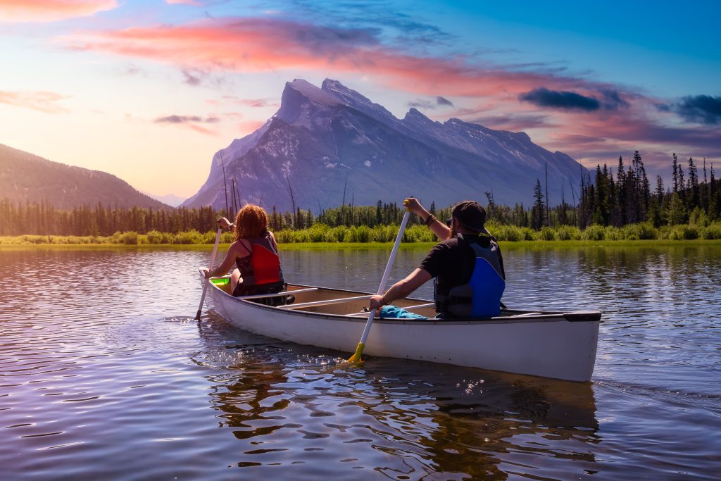 adventurous friends are canoeing in a lake surrounded by the canadian mountains