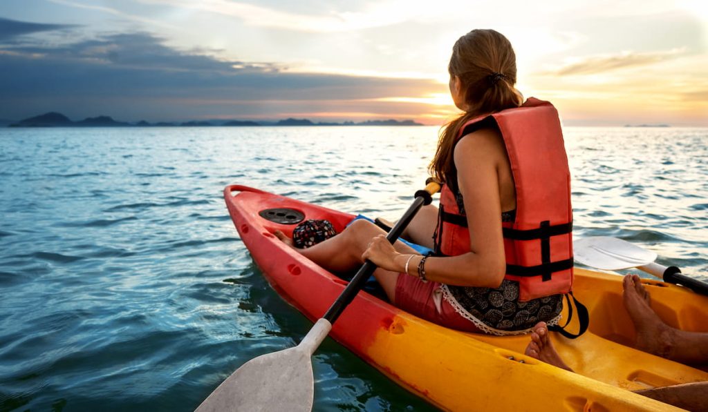 young woman wearing life jacket kayaking on lake 
