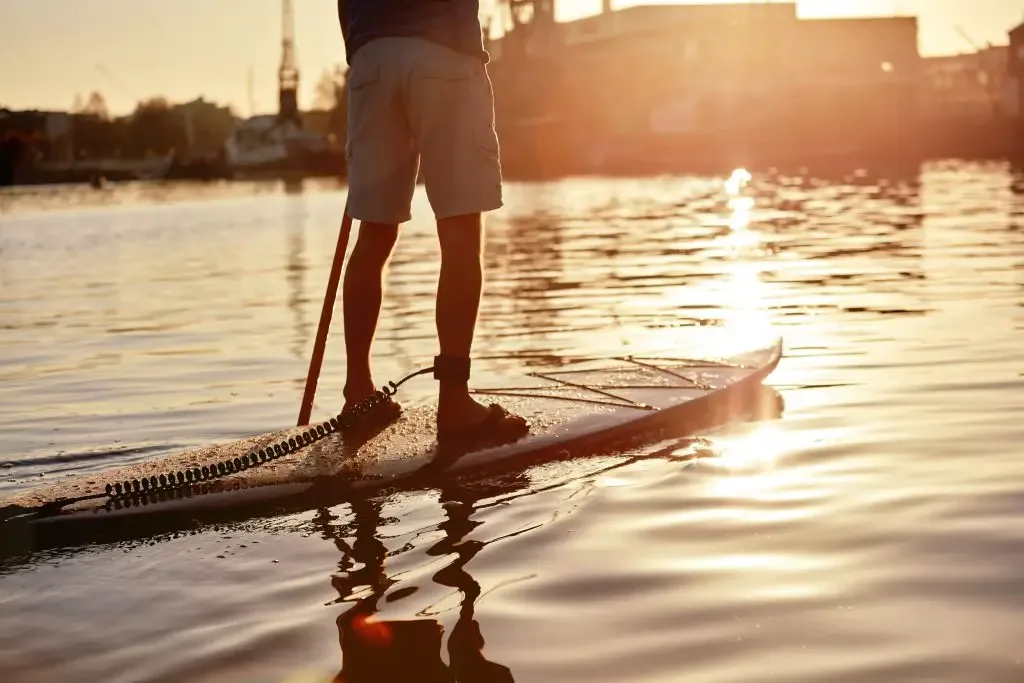 man standing on paddleboard on river at dawn