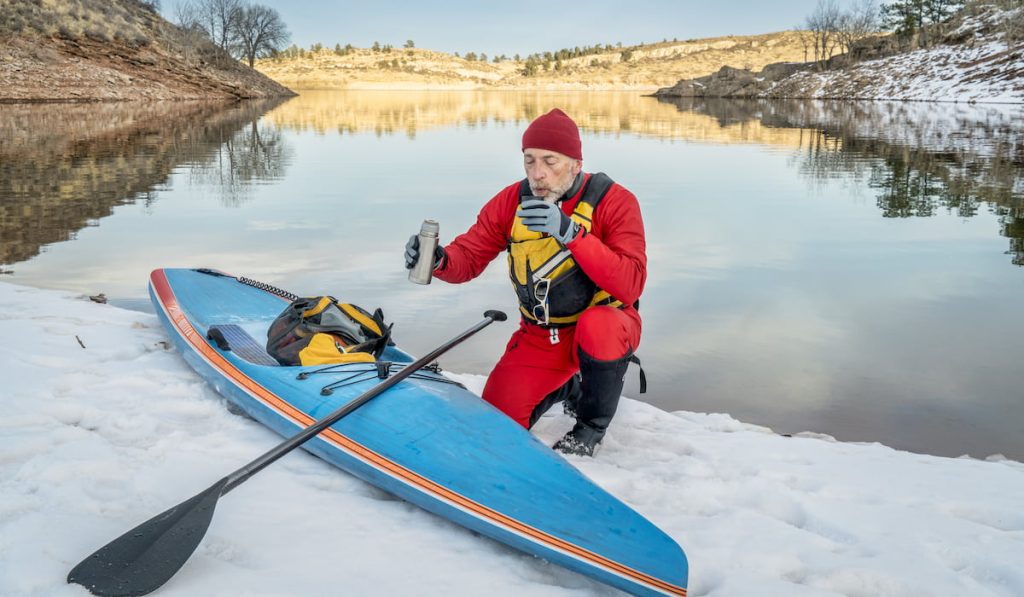 man sipping a hot coffee after paddleboarding during winter