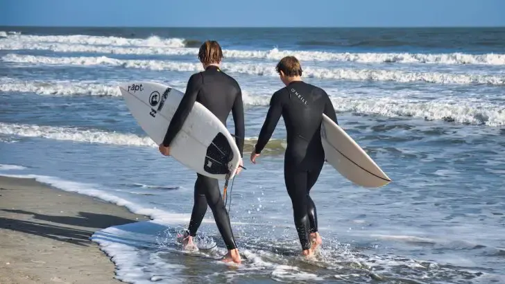 two surfers are walking together on the beach