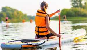 woman wearing life jacket sitting on a paddleboard